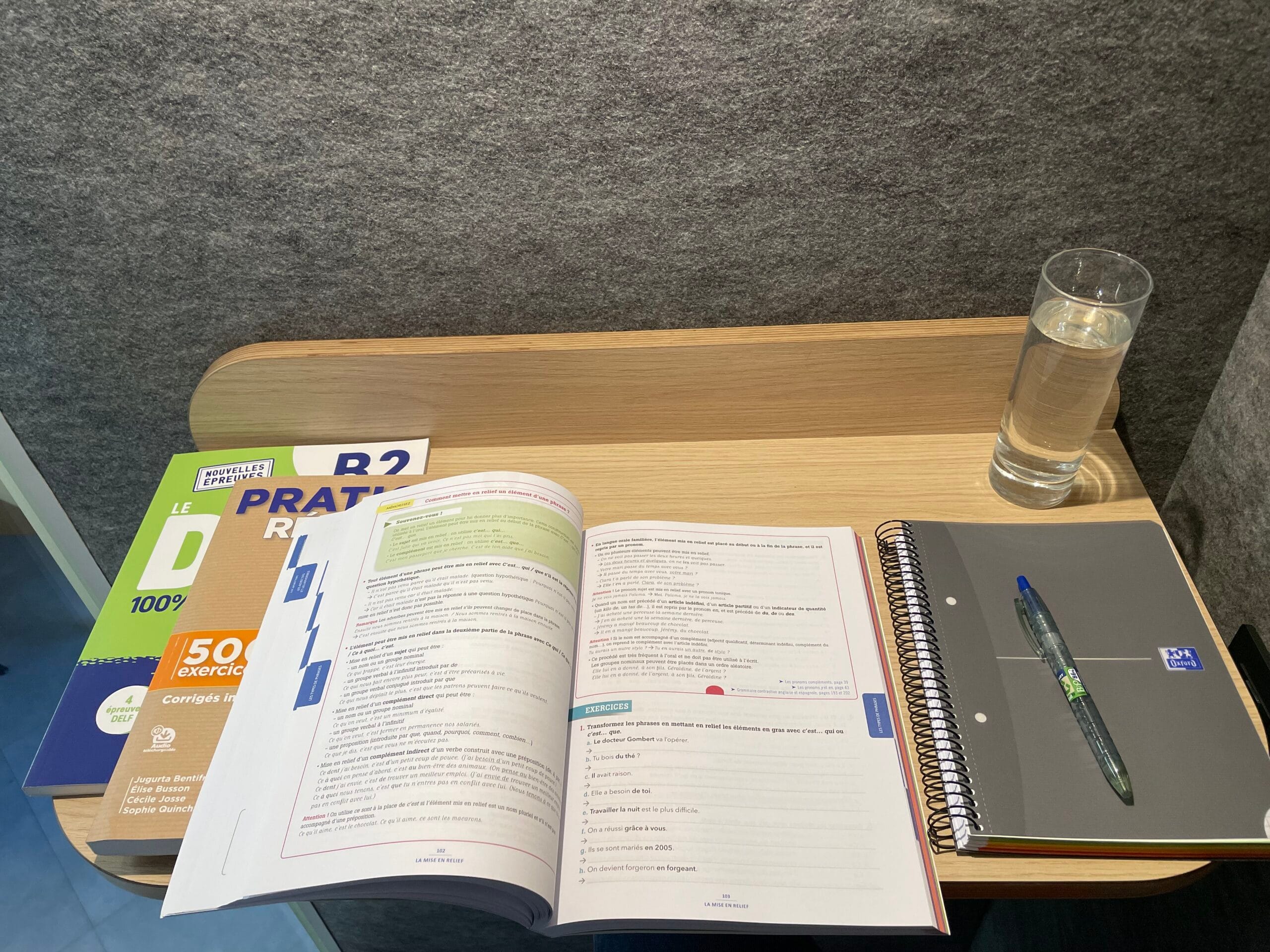 Open French grammar book on study desk with notebook and water glass — FTC Paris quiet zone